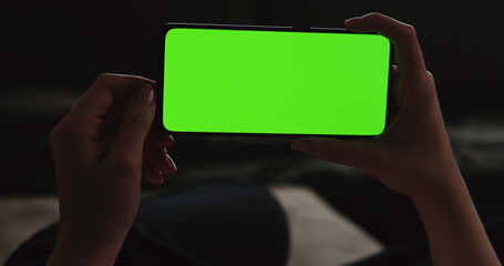 Young woman lying on a couch and using smartphone with horizontal green screen