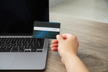Woman with credit card using laptop at wooden table indoors, closeup