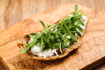 crunchy rustic bread with ricotta and arugula on olive wood board