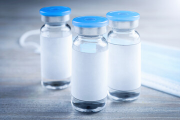 Medication in glass vials and medical mask on wooden table, closeup