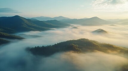 Obraz premium A serene aerial view of mountains shrouded in mist at sunrise, showcasing nature's beauty and tranquility.