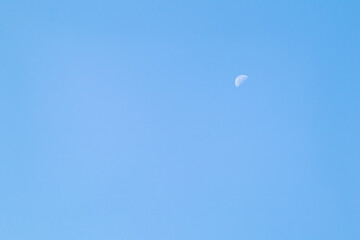 A beautiful crescent moon in the afternoon sky. A crescent moon in daylight against a clear blue sky.