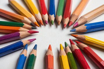 Scattered colored pencils in a circular arrangement on white