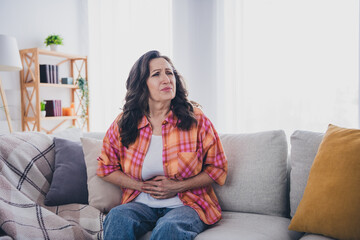 Photo of sick upset woman dressed checkered shirt feeling stomach ache indoors house apartment room