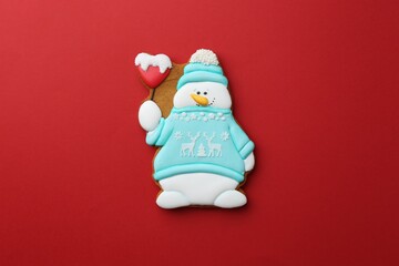 Tasty Christmas cookie in shape of snowman on red background, top view
