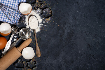 spoon with flour and baking ingredients on a black background, top view
