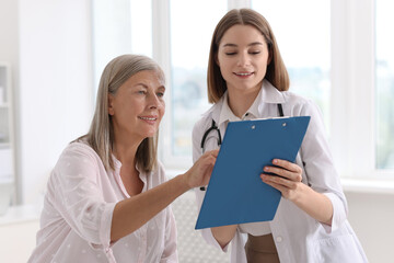 Smiling healthcare worker with clipboard consulting senior patient in hospital