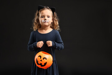 Fototapeta premium Cute girl with pumpkin bucket dressed like cat for Halloween celebration on black background, space for text