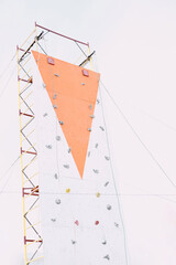 Outdoor climbing wall on tall scaffolding with colorful holds against bright sky.