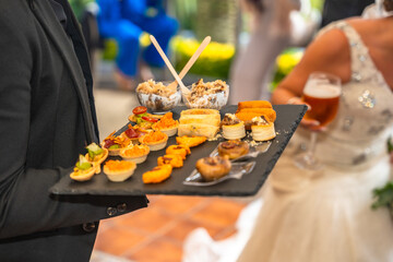 A man is holding a tray of food, including a variety of appetizers and desserts