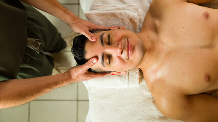 Top view of a male massage therapist giving a head massage to a relaxed client on a spa table