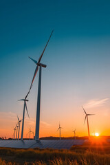 Obraz premium A scenic view of wind turbines and solar panels during sunset. The sky is painted with warm hues of orange and blue, creating a tranquil atmosphere.