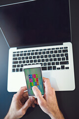 Man, hands and phone by laptop for communication, social media or website at office desk. Creative person, screen and computer for freelance, mobile app design or UX test for startup technology