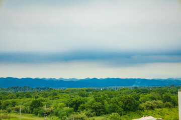 A beautiful mountain landscape with green fields, trees, and fluffy clouds under a bright sun