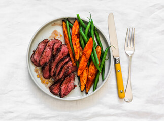 Medium-rare beef steak, sweet potato, string beans - a delicious lunch on a light background, top view