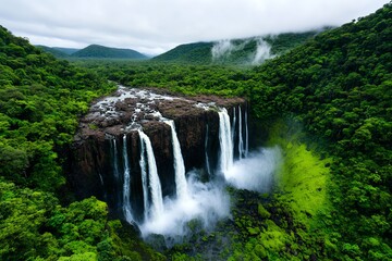 Naklejka premium A majestic waterfall cascading down a rocky cliff, surrounded by lush green vegetation and mist rising from the water