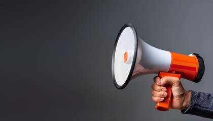 Close-up of a hand holding a megaphone against a gray background, symbolizing communication, announcement, and spreading information.