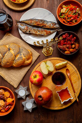 Challah, honey, apple and pomegranate and wine and chelnt with dried fruits on the table with menorah in honor of Rosh Hashanah