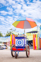 A colorful ice cream cart with a rainbow umbrella, set against a bright blue sky. The vibrant street food vendor cart stands out at an outdoor festival, inviting people to enjoy a cool treat. © nutt