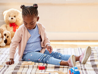 Toddler, playing and building blocks in game for growth, development and learning for motor skills. African child, toys and puzzle in education, creativity or fun for cognitive ability in family home