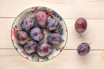 Ripe plums in a ceramic dish on a wooden table, macro, top view.