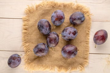 Obraz premium Ripe plums on a jute napkin on a wooden table, macro, top view.