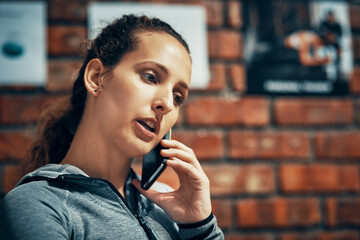 Face, fitness and phone call with personal trainer woman in gym for communication or networking. Brick wall, exercise and workout coach talking on mobile for membership offer or recruitment