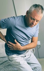 Obraz premium Young adult man with back pain.Man with kidney pain.Kidney stones.Sciatica.Low back.Boy complaining of back pain.Man struggling to get out of bed,because of back pain.Man trouble waking up.