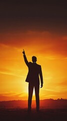 Fototapeta premium Silhouette of a man in a suit pointing upwards against an orange sunset, symbolizing ambition and aspiration.