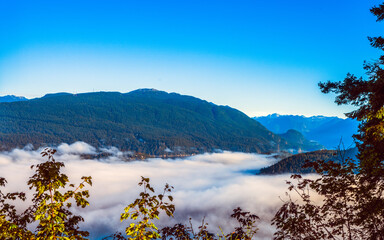 Dense cloud inversion over Burrard Inlet, BC, with forested mountain backdrop,.