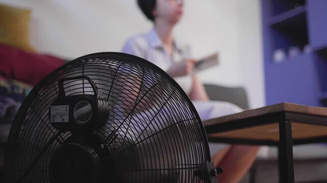 Woman gets hot indoors at summer. Young woman using floor fan to cool down.
