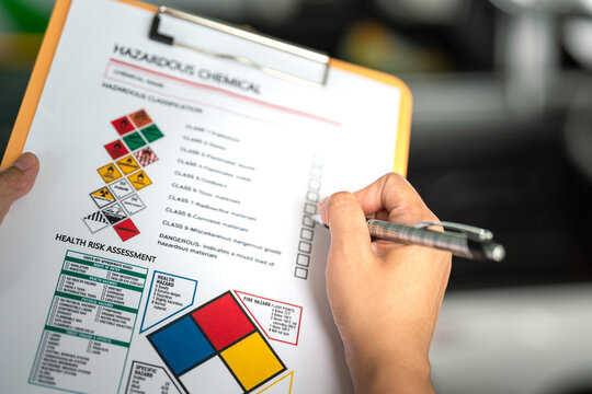 Action of a safety officer is marking on the chemical hazard material checklist to verify the type of risk at the chemical factory plant. Industrial working safety scene, close-up.