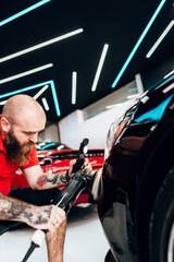Professional vehicle polishing and detailing service in a modern car workshop. Brightly lit workspace with large led lights. High quality car valeting concept.