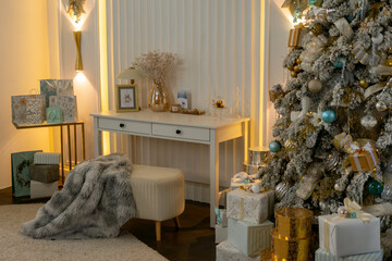 A white Christmas tree with gold and blue decorations sits in front of a white desk. The desk is...