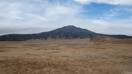 Mount Aso, A view of a volcano in Japan, with some smoke billowing out, and many horses grazing.