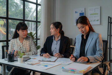 Three young businesswomen working together on a project, analyzing financial charts and reports. They are having a productive meeting in a modern office
