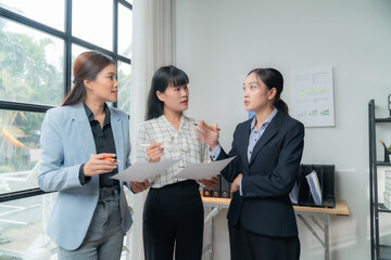 Three confident asian businesswomen discussing documents in a modern office, brainstorming ideas...