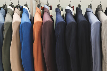A row of suits hanging on a rack, with the blue suit on the far left and the brown suit on the far...