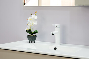 A white sink with a white faucet and a white flower pot with a white flower in it
