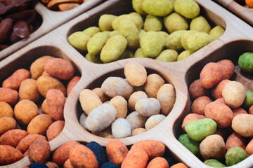 A wooden tray with a variety of nuts and seeds. The tray is filled with different colored nuts and seeds, including green, brown, and white. The nuts and seeds are scattered throughout the tray