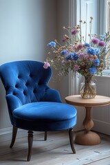 Indigo blue velvet armchair and ottoman, small round side table with a vase of flowers in the corner, light gray walls. Interior design