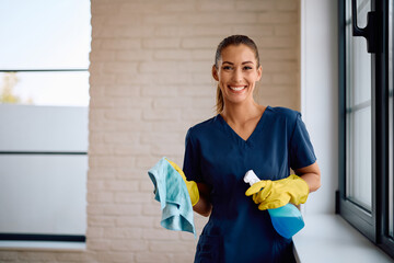 Happy woman cleaning windows at home and looking at camera.