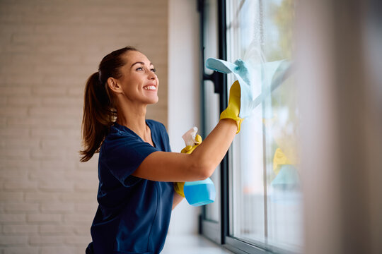 Young happy woman cleaning window glass at home. Copy space.