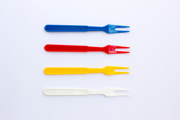 Several small plastic forks are isolated on a white background. These forks are colored red, yellow, blue. 