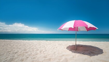 A pink and white beach umbrella stands alone on a sandy beach with the ocean in the background.