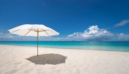 A single white umbrella stands on a sandy beach, casting a shadow on the pristine sand. The turquoise sea stretches out under a clear blue sky with fluffy white clouds.