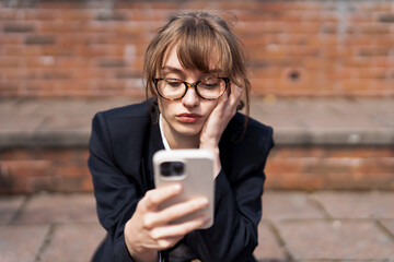 Young Woman in Formal Outfit Checks Her Phone While Sitting on Steps in Urban Setting