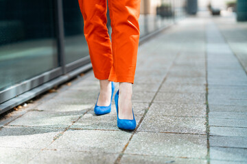 Confident Woman Walks Down City Sidewalk in Bright Orange Pants and Blue Heels