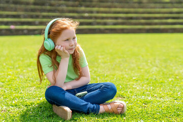 Fototapeta premium Young Girl Enjoying Moment of Reflection in Sunlit Park While Listening to Music