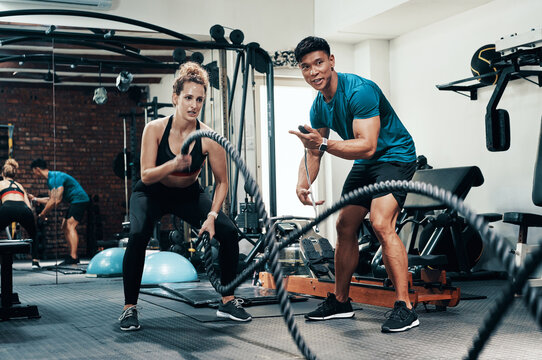 Fitness, battle ropes and woman in gym, training and personal trainer with timer, energy and sweat. Health club, exercise and endurance for cardiovascular conditioning, people and wellness of workout